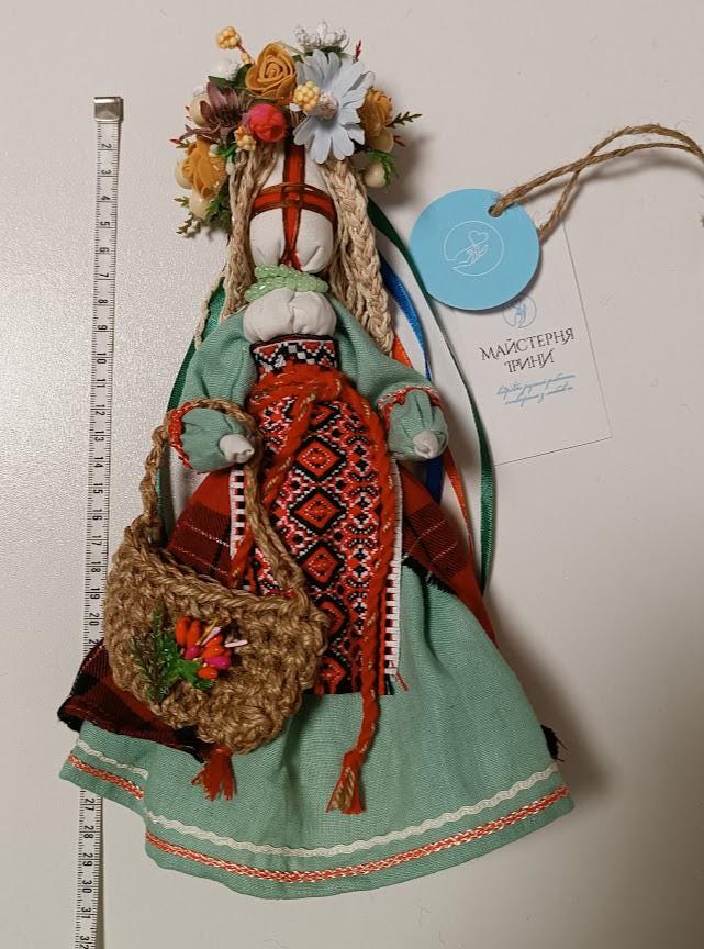 Traditional Ukrainian Motanka doll with colorful dress and floral headpiece, standing beside a measuring tape.
