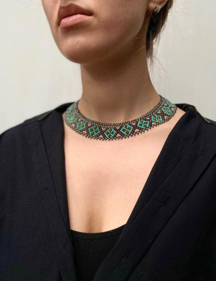 Woman wearing handmade Ukrainian Sylyanka necklace with ceramic and turquoise beads, featuring ethnic geometric patterns.