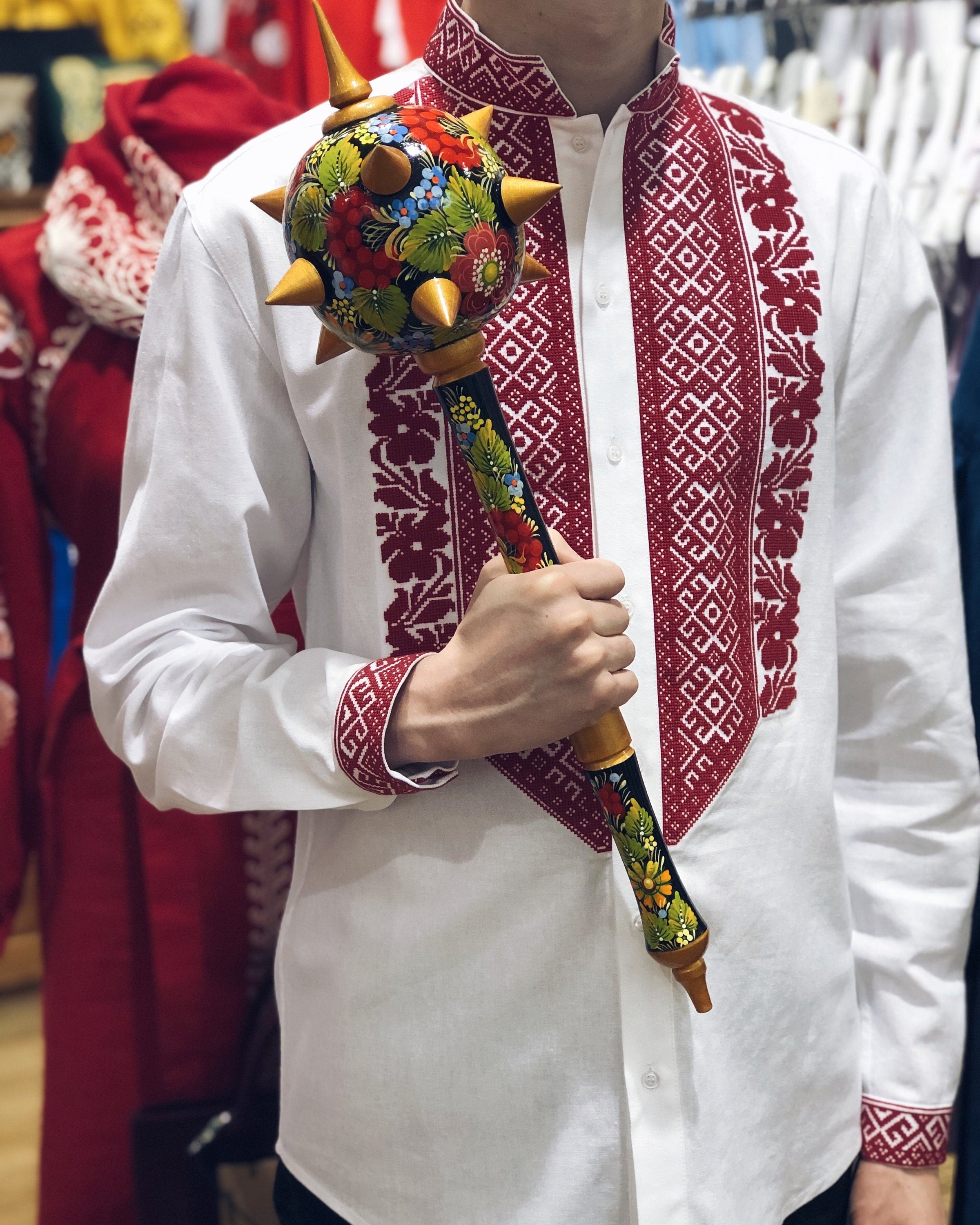Man holding handmade wooden Ukrainian Bulava mace, a traditional Cossack symbol, in embroidered shirt, perfect cultural gift for him.