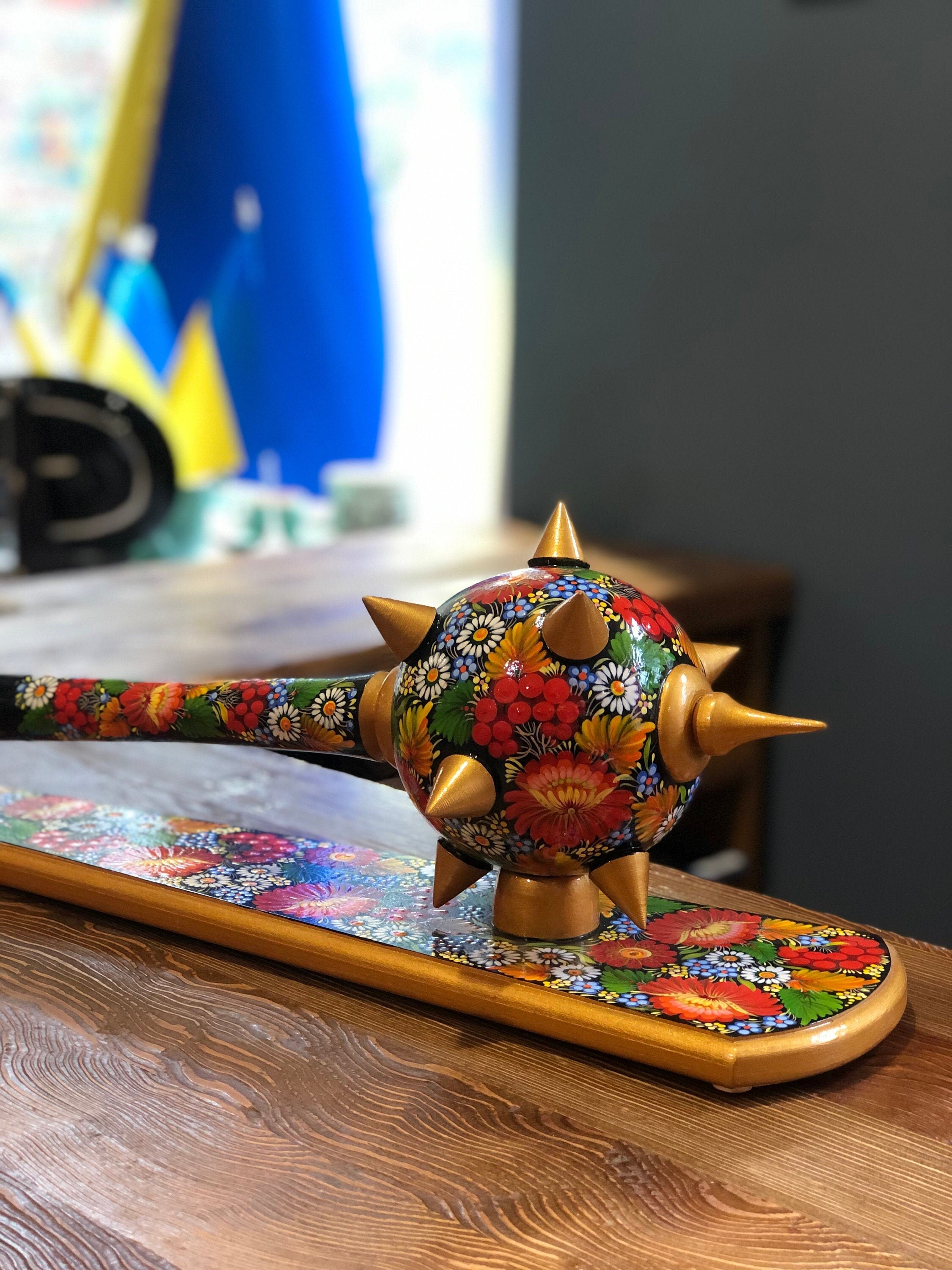 Handmade wooden Ukrainian Bulava with floral design, symbolizing leadership and cultural heritage, displayed on wooden surface.