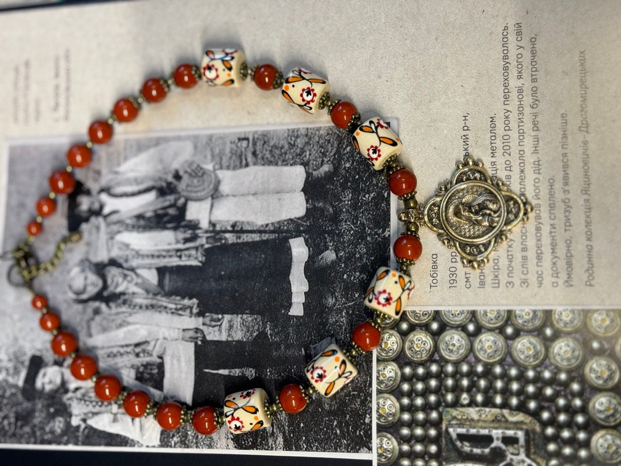 Handmade Ukrainian necklace with white clay and jasper beads, featuring cast brass pendant on a vintage book background.
