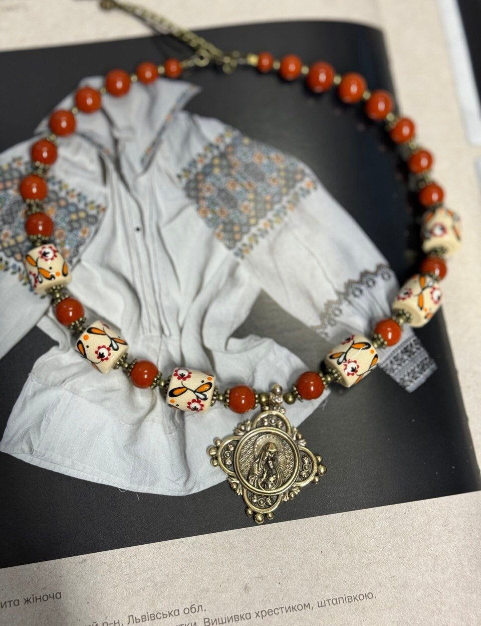 Handmade Ukrainian necklace with white clay and jasper beads on traditional embroidered fabric background.