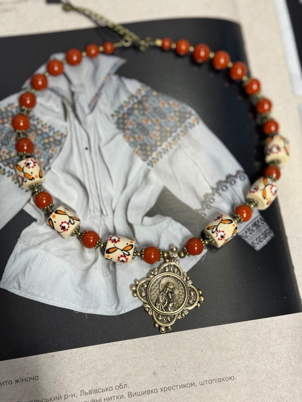 Handmade Ukrainian necklace with white clay and jasper beads on traditional embroidered fabric background.