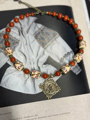 Handmade Ukrainian necklace with white clay and jasper beads on traditional embroidered fabric background.