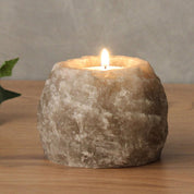Himalayan salt candle holder emitting a warm amber glow, handcrafted for meditation and relaxation, on a wooden surface.