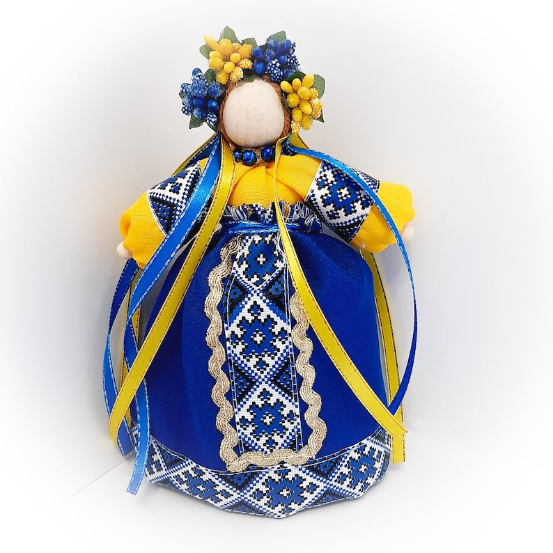 Ukrainian Motanka doll with blue and yellow dress, decorated with floral wreath, representing home protection and housewarming gift.