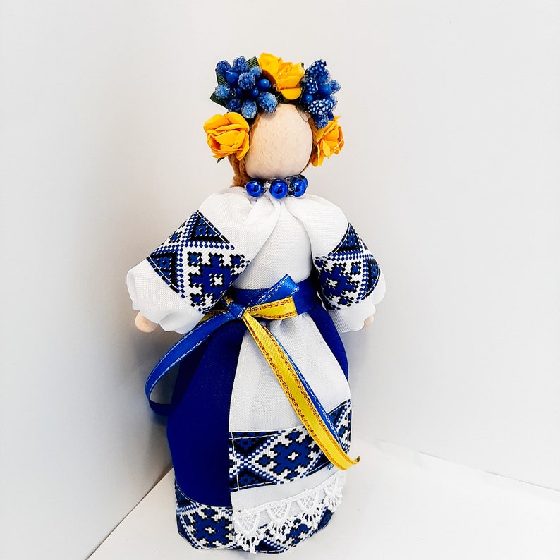 Ukrainian Motanka doll in blue and white traditional attire, with floral headpiece and yellow-blue ribbon, symbolizing cultural heritage.