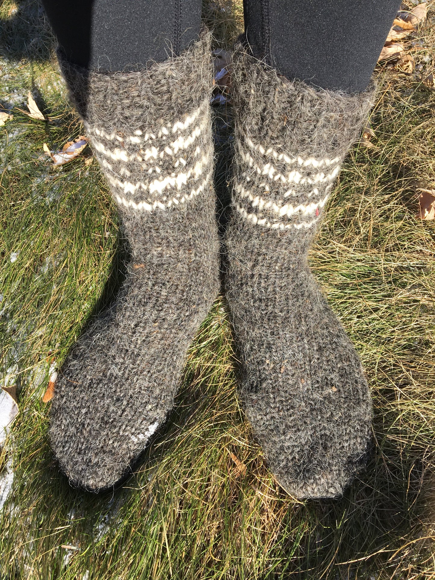 Hand-knitted wool socks made from pure sheep wool, unisex winter wear displayed outdoors on grass.