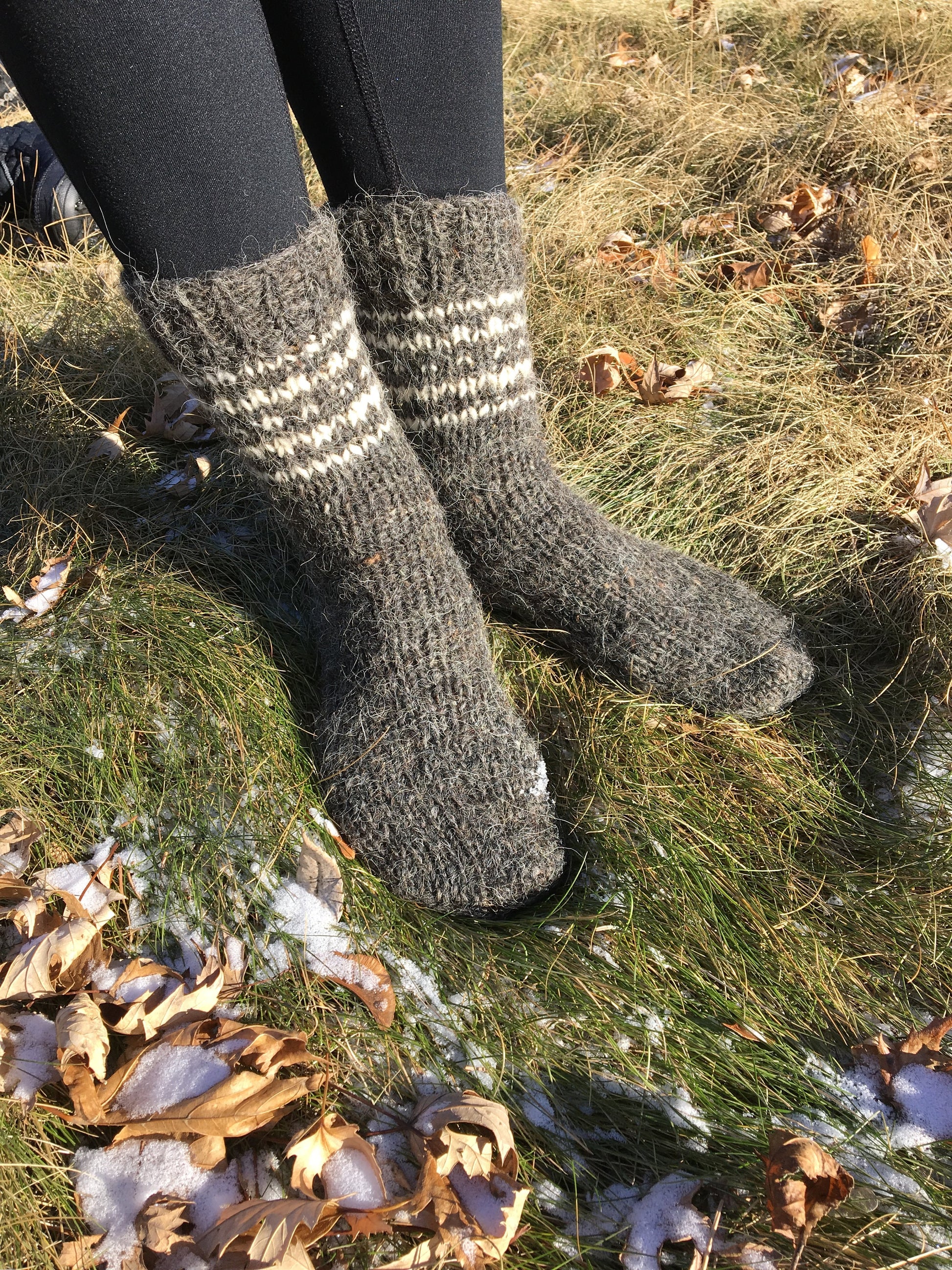 Unisex hand-knitted wool socks in grey, made from pure sheep wool, worn outdoors on grass in winter.