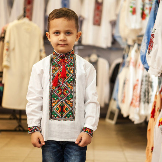 Boy wearing a traditional Ukrainian Vyshyvanka embroidered linen shirt, featuring colorful patterns on chest and cuffs, in a clothing store.