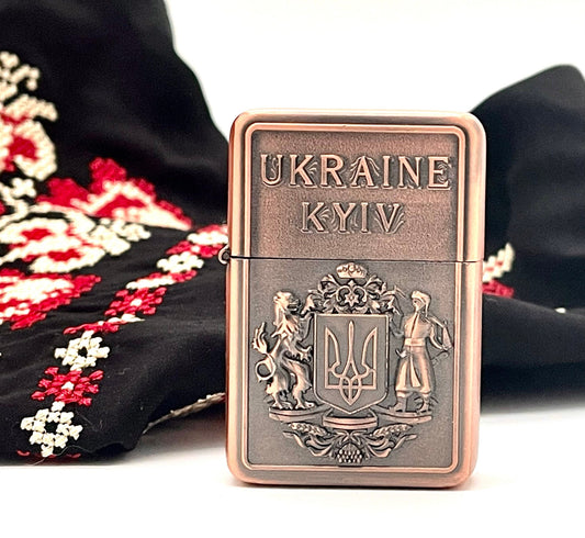 Ukrainian gasoline lighter with bronze and silver Coat of Arms, Kyiv inscription, and embroidered fabric backdrop.