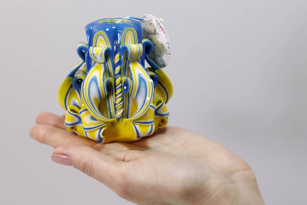 Handcrafted blue and yellow carved candle on a hand, symbolizing support for Ukraine and aid for war-affected families.