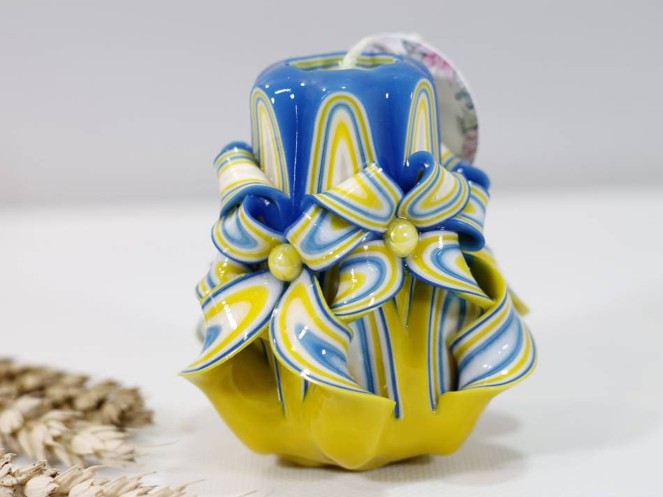 Handcrafted blue and yellow carved candle symbolizing support for Ukraine with elegant flower design.