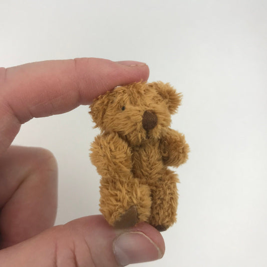 Hand holding tiny soft fuzzy stuffed teddy bear with moveable arms and legs, perfect for decoration or as a miniature gift.