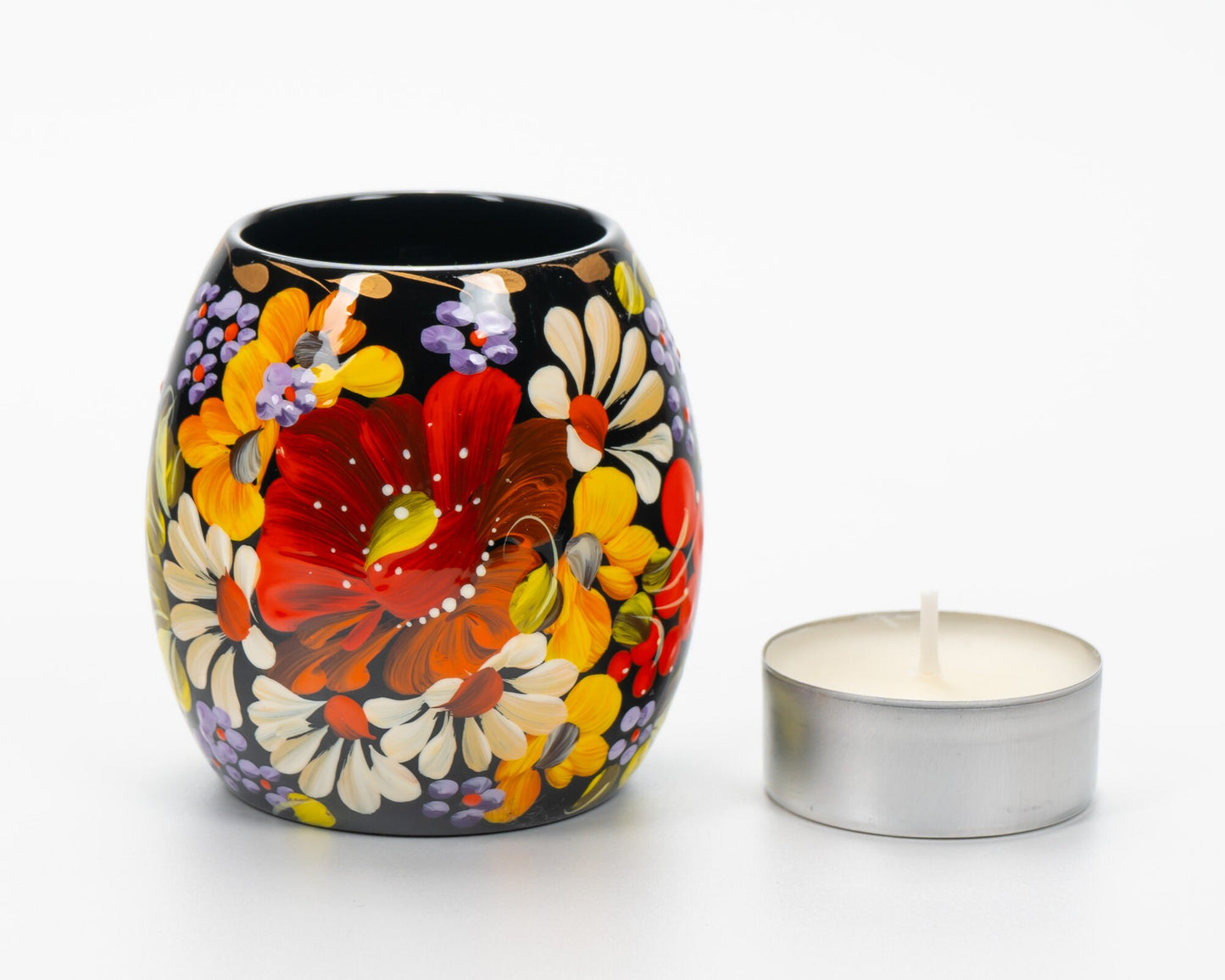 Hand-painted Ukrainian tea light candle holder with Petrykivka floral design beside white candle.