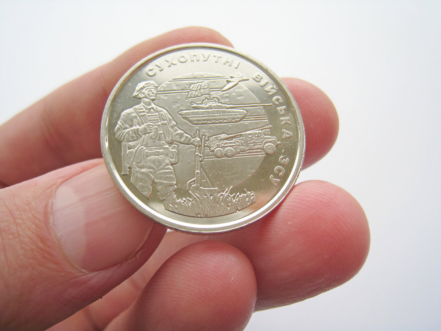 Ukrainian 10 Hryvnia 2021 commemorative coin honoring Land Forces held between fingers, showcasing detailed emblem and design.