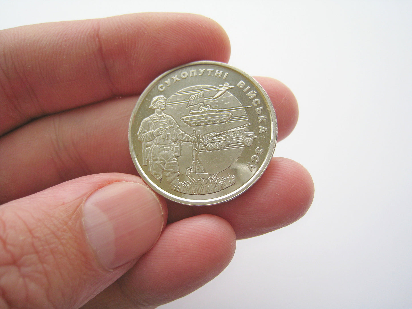 Close-up of a 2021 Ukrainian 10 Hryvnia commemorative coin featuring the Land Forces emblem, held between fingers.