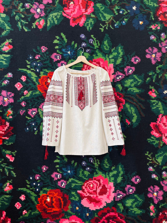 Authentic Ukrainian Vyshyvanka blouse with intricate embroidery, hanging against a vibrant floral background.