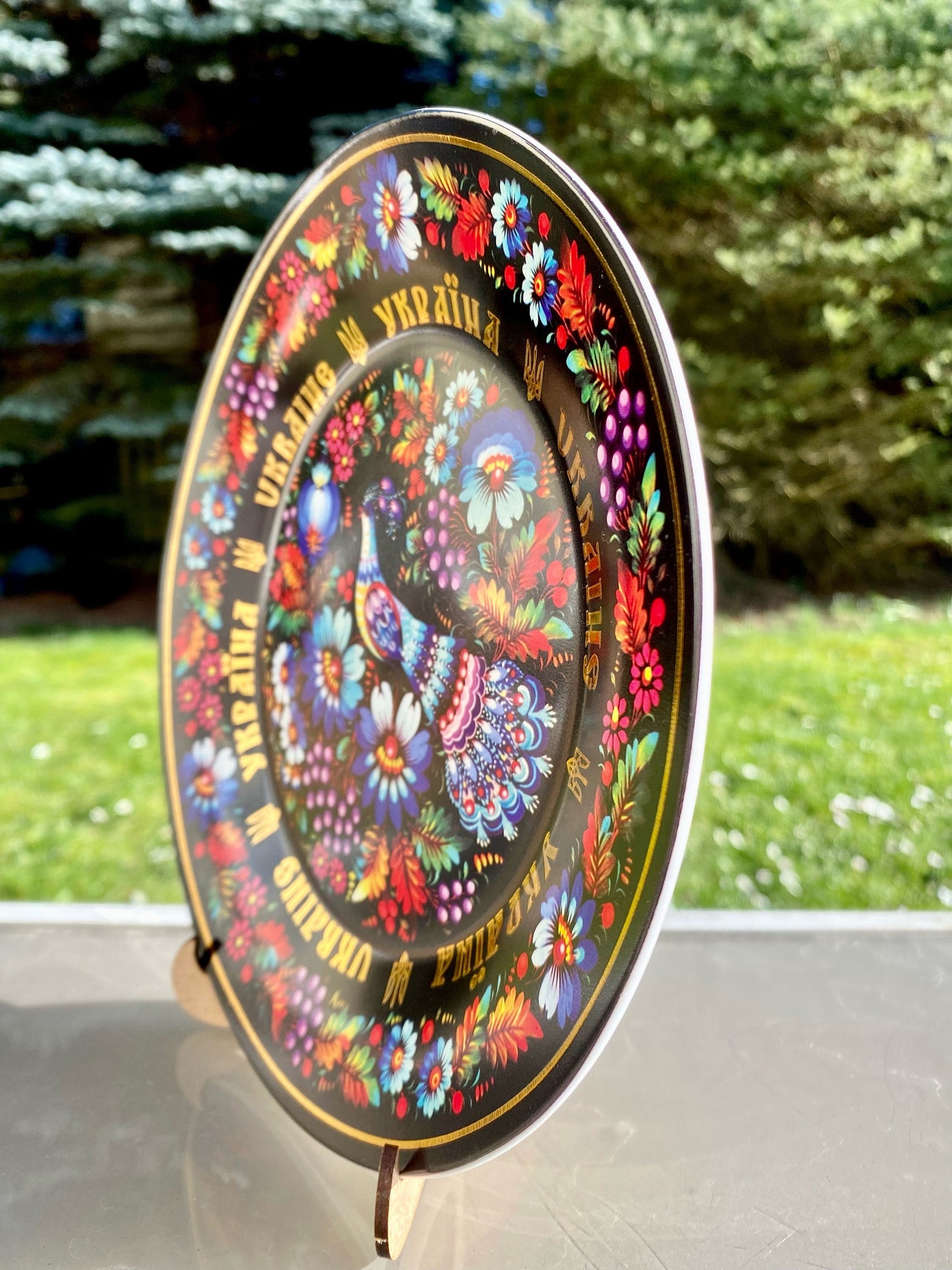 Ukrainian porcelain plate with Petrykivsky pattern on wooden stand, featuring vibrant floral design, displayed outdoors.