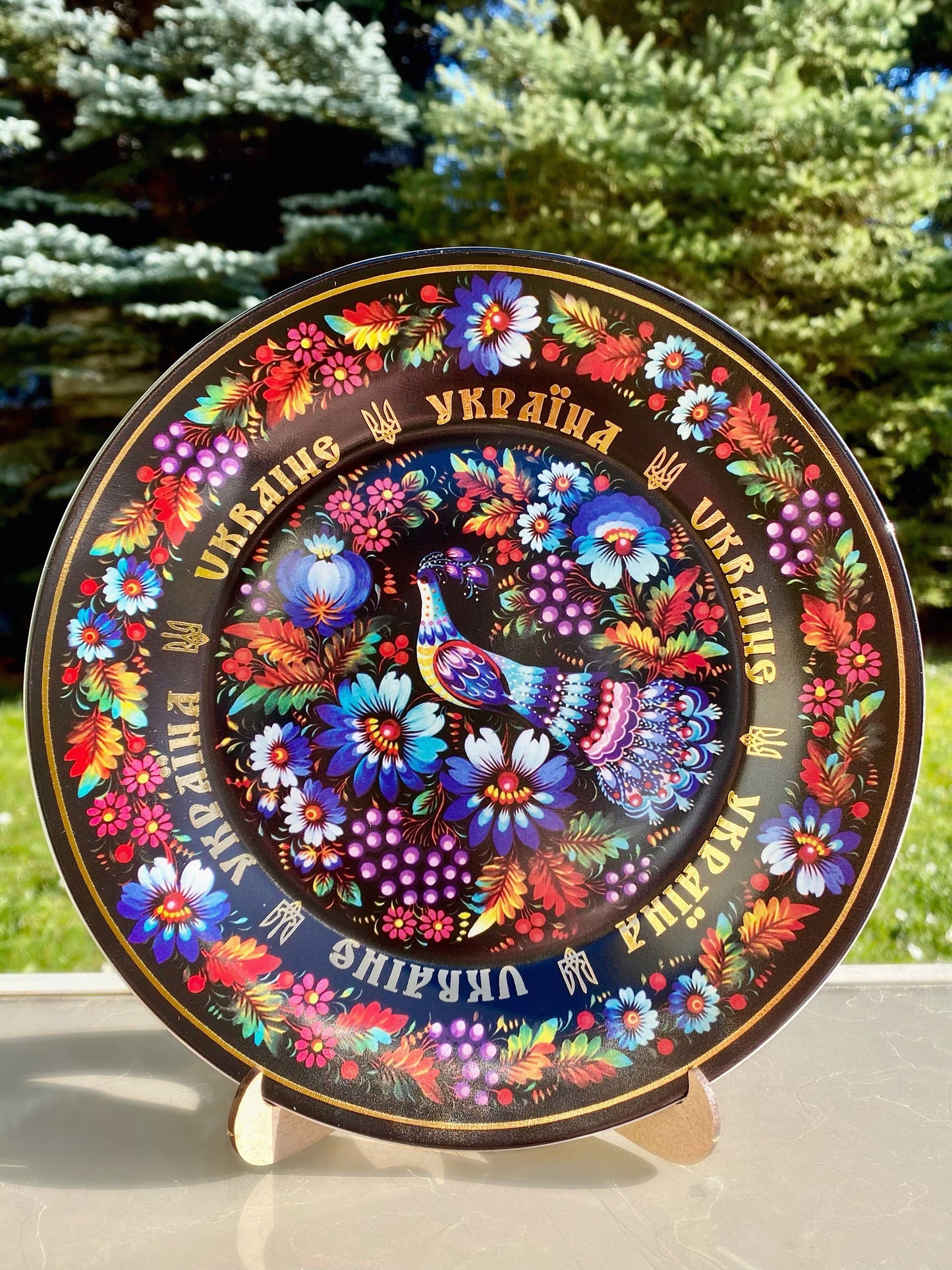 Ukrainian porcelain plate with vibrant Petrykivsky floral pattern on a wooden stand.