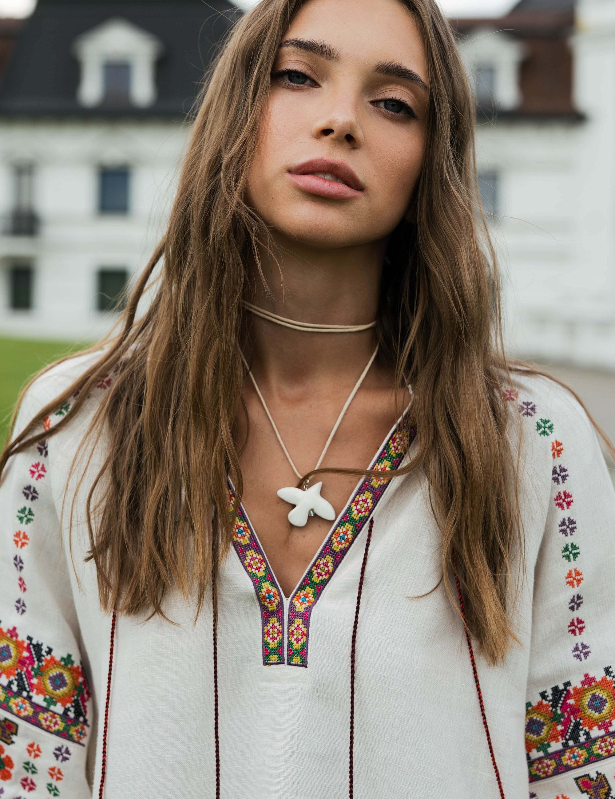 Woman wearing a soft beige linen Vyshyvanka blouse with Ukrainian embroidery, featuring floral and geometric motifs, in a serene outdoor setting.