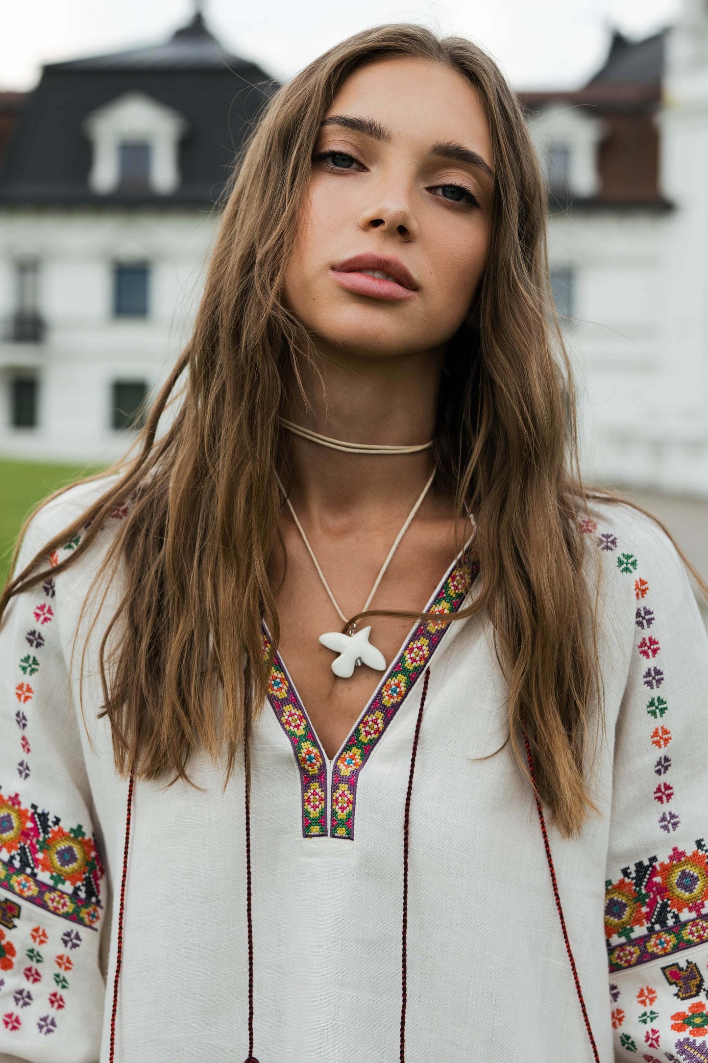 Woman wearing a beige linen Vyshyvanka blouse with colorful Ukrainian embroidery, standing outdoors.