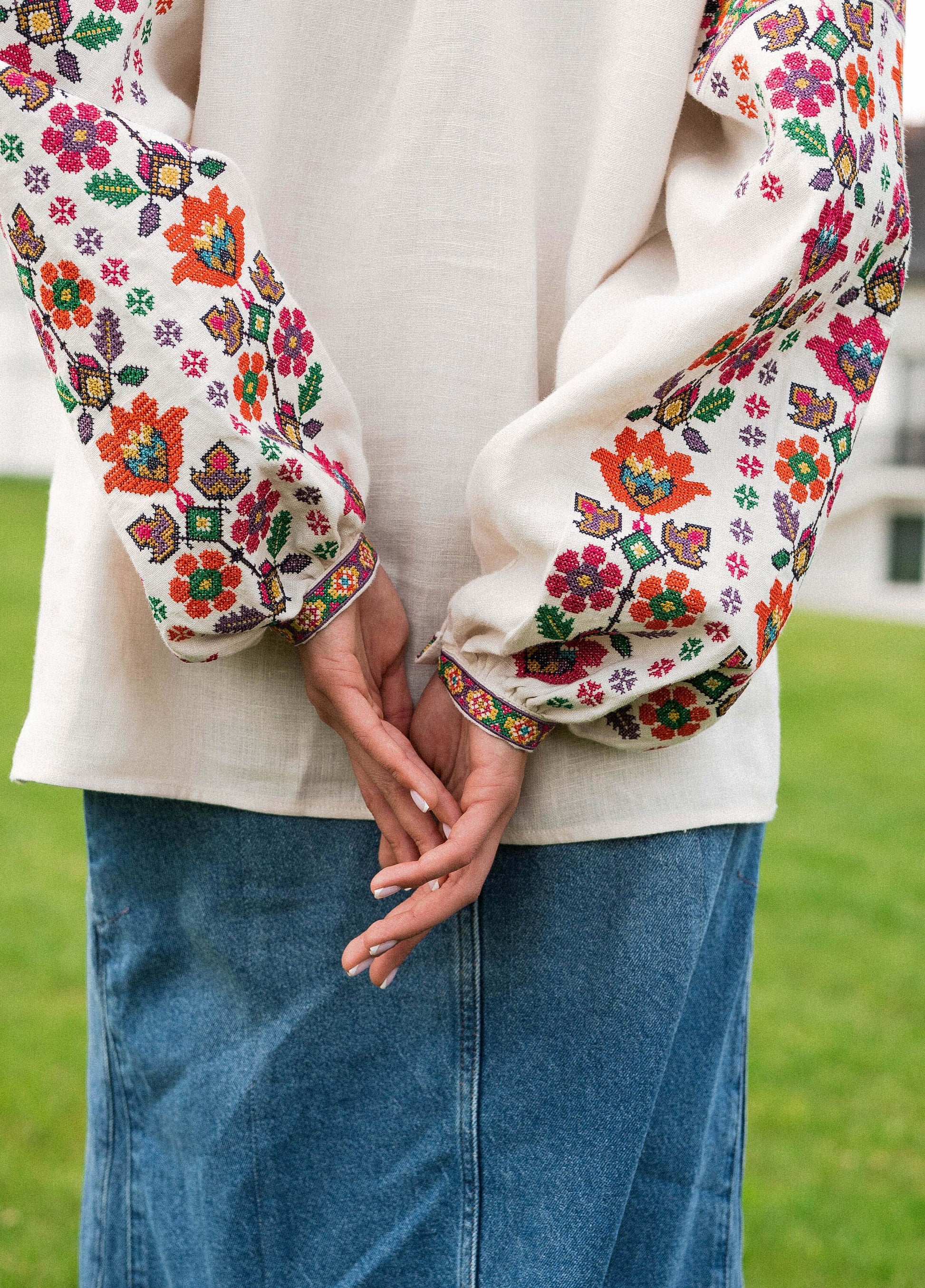 Beige linen blouse with colorful Ukrainian embroidery on sleeves, showcasing geometric and floral patterns.