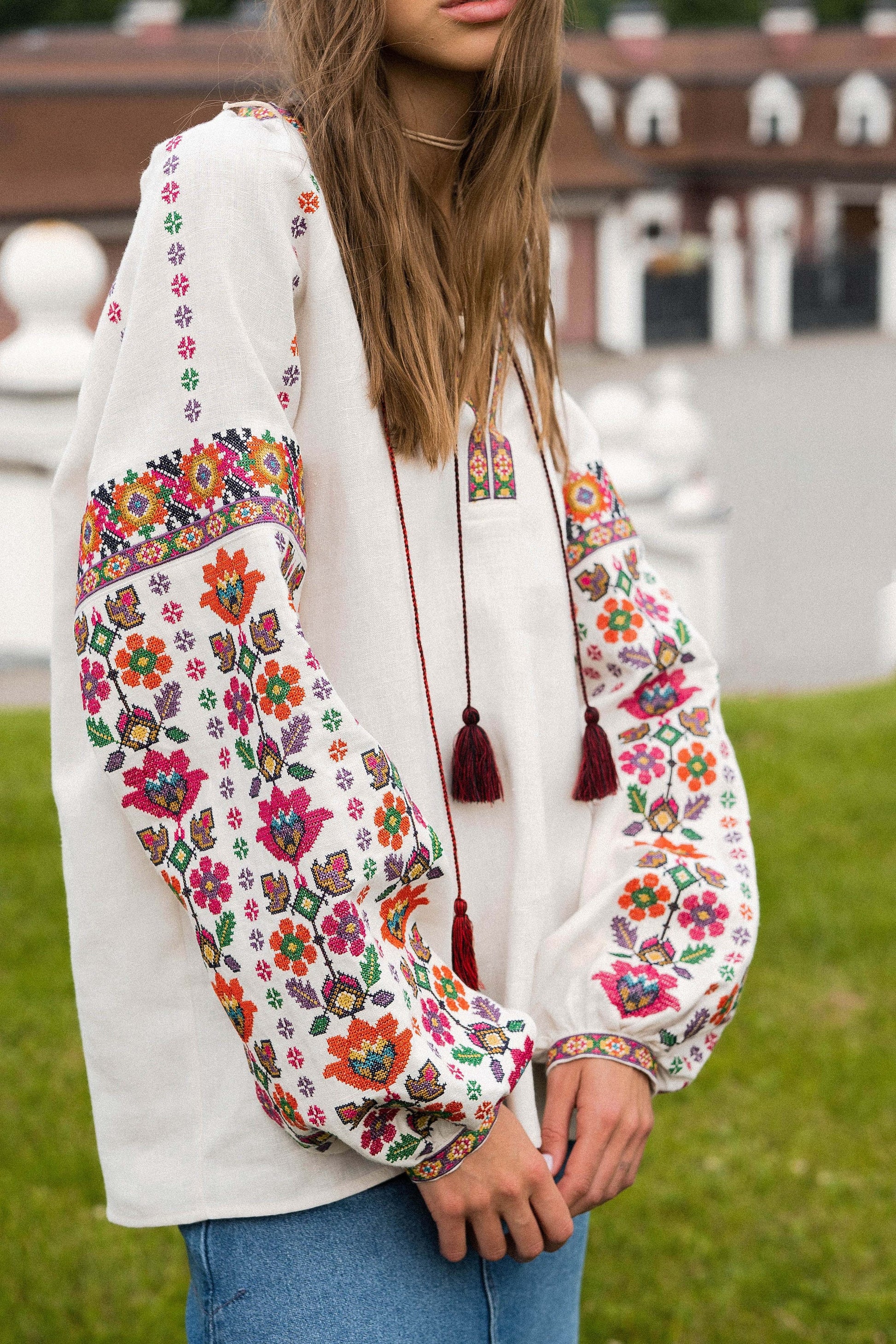 Woman wearing a beige linen Vyshyvanka blouse with vibrant floral embroidery, standing outdoors.