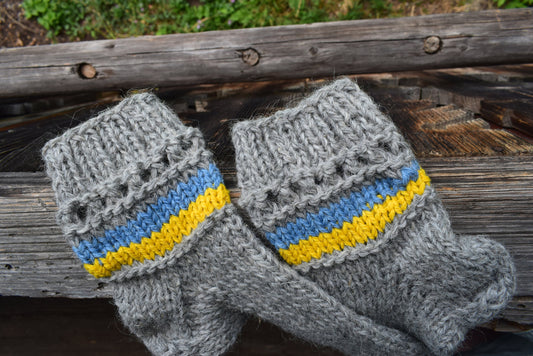 Hand-knitted grey woolen socks with Ukrainian flag colors on wooden background, made from 100% natural wool.