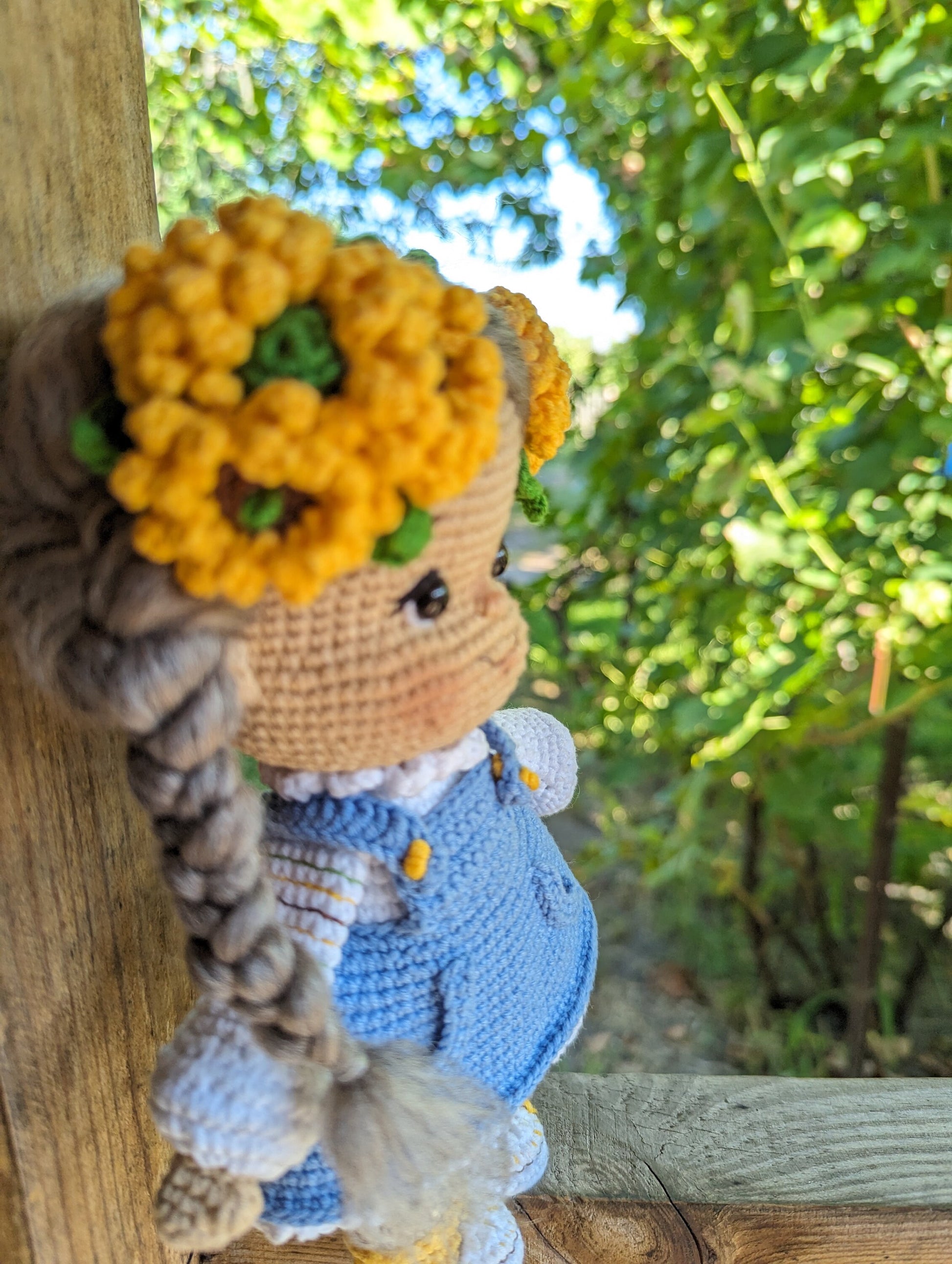 Crochet Ukrainian doll in blue dress with yellow flower crown, folk-style soft toy, against a green leafy background.