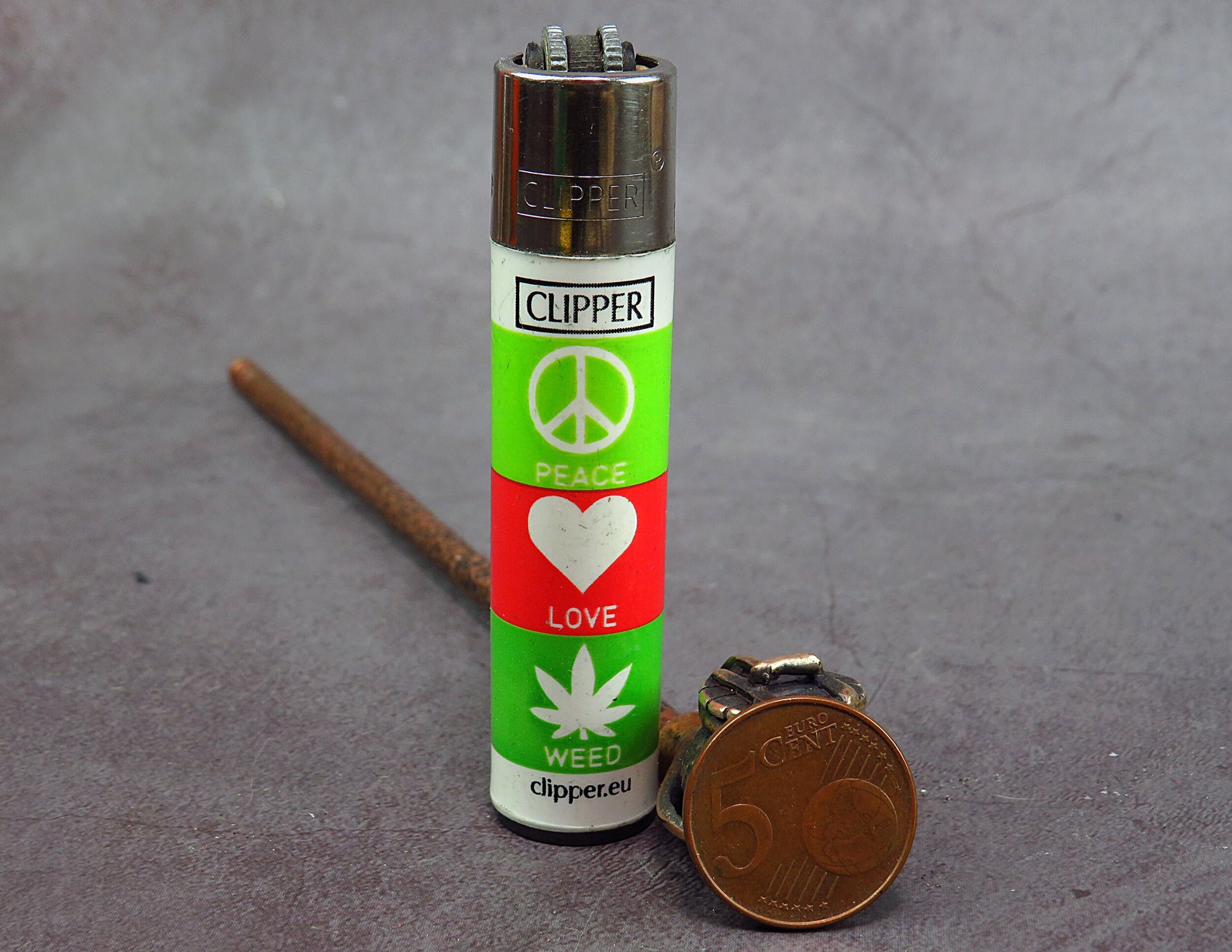 Clipper lighter with peace and love symbols, alongside rustic bronze pipe and coin.