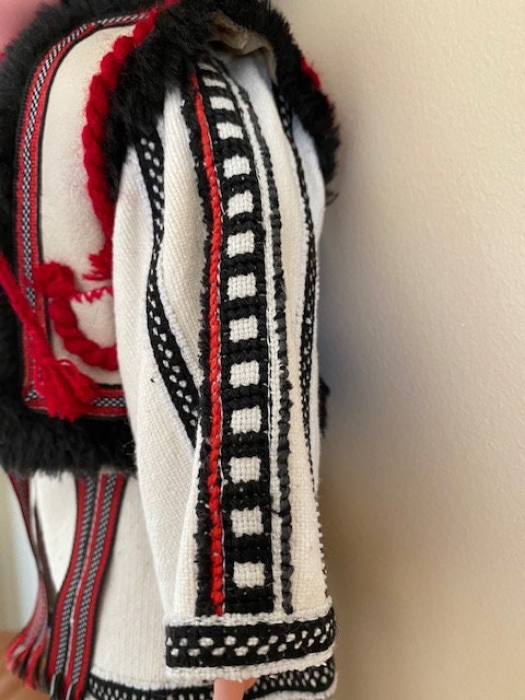 Hand-embroidered detail on Ukrainian boy doll's traditional Carpathian outfit, featuring black, red, and white patterns.