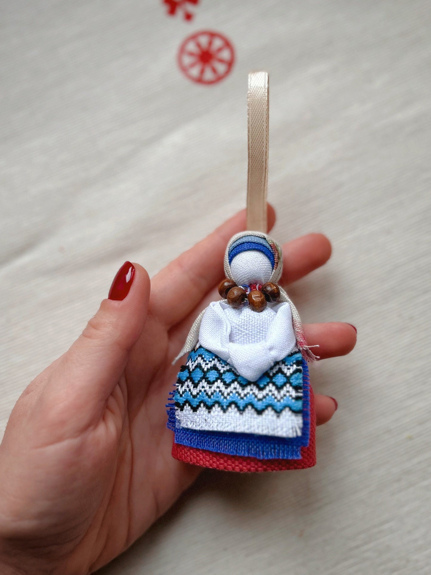 Hand holding Motanka Ukrainian Doll "Little Bereginiya" with colorful folk attire and ribbon loop, symbolizing luck and protection.