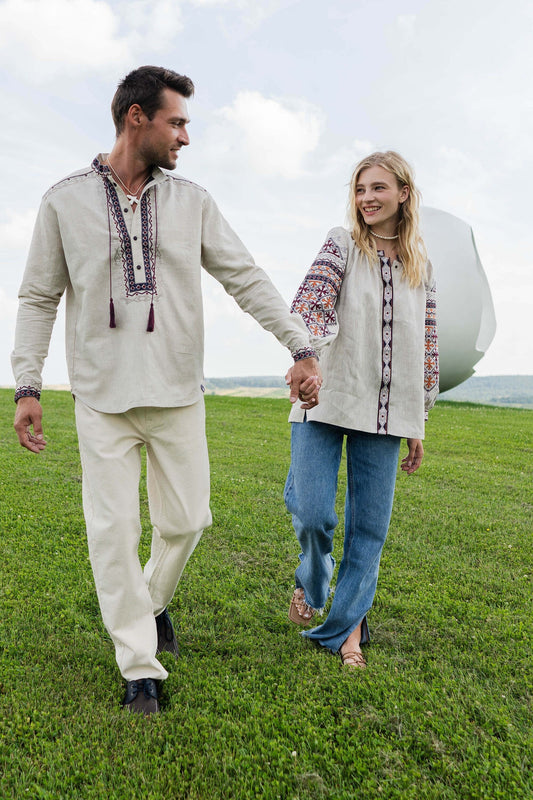 Couple wearing traditional Vyshyvanka embroidered shirts walking on a sunny day in a green field.