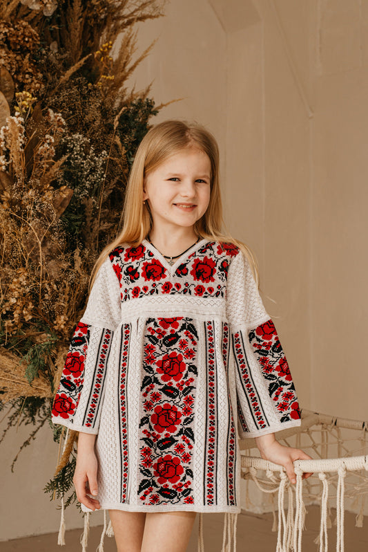 Girl in Ukrainian embroidered knit dress with red floral design, traditional Vyshyvanka style, cotton clothing for children.