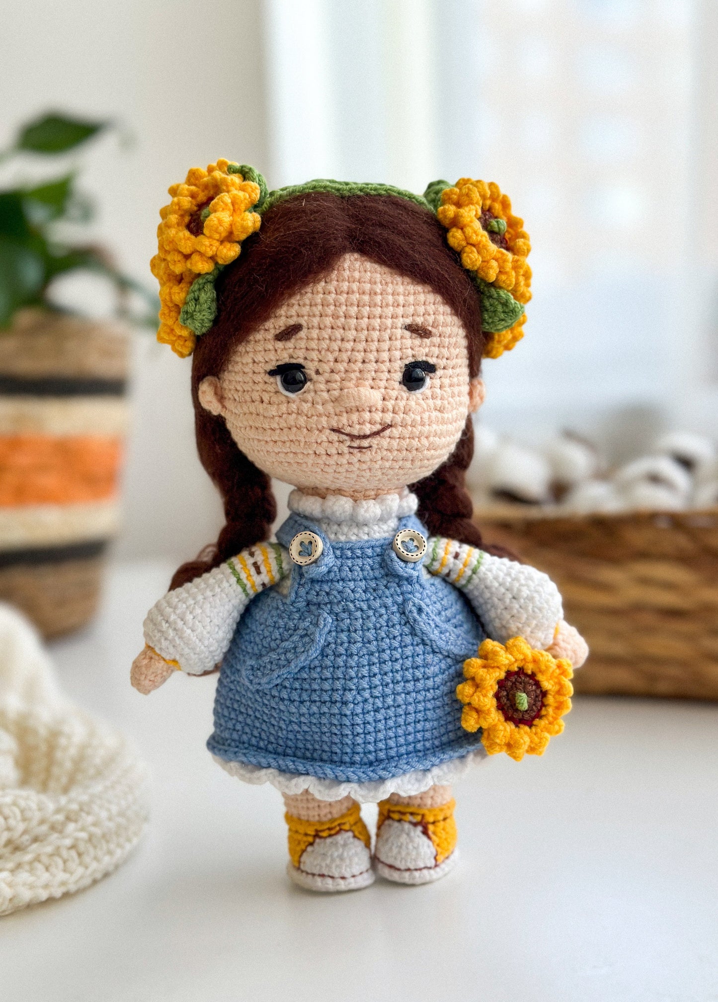 Handmade knitted doll with sunflower decorations, wearing a blue dress, on a cozy indoor background. Perfect Ukrainian-themed gift.