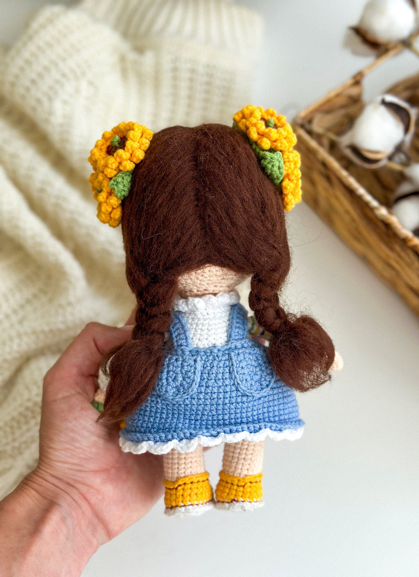 Handmade knitted doll with flowers in hair, wearing a blue dress, held in hand, showcasing intricate Ukrainian-themed details.