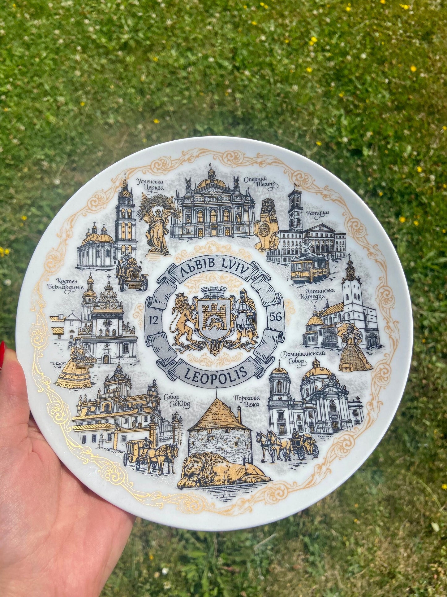 Lviv bronze-style porcelain wall plate with iconic landmarks, decorative souvenir, 20cm, held against a grassy background.