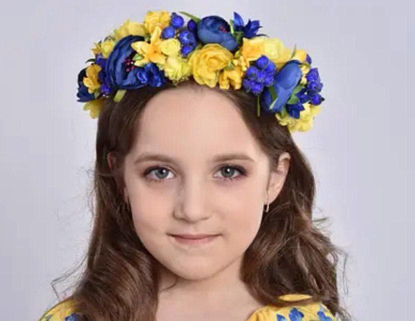 Girl wearing floral Ukrainian headband with yellow and blue flowers, cultural fashion accessory.