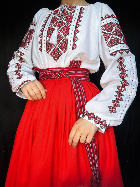 Traditional Ukrainian Vyshyvanka blouse with red cross-stitch embroidery on white fabric, paired with a red skirt.