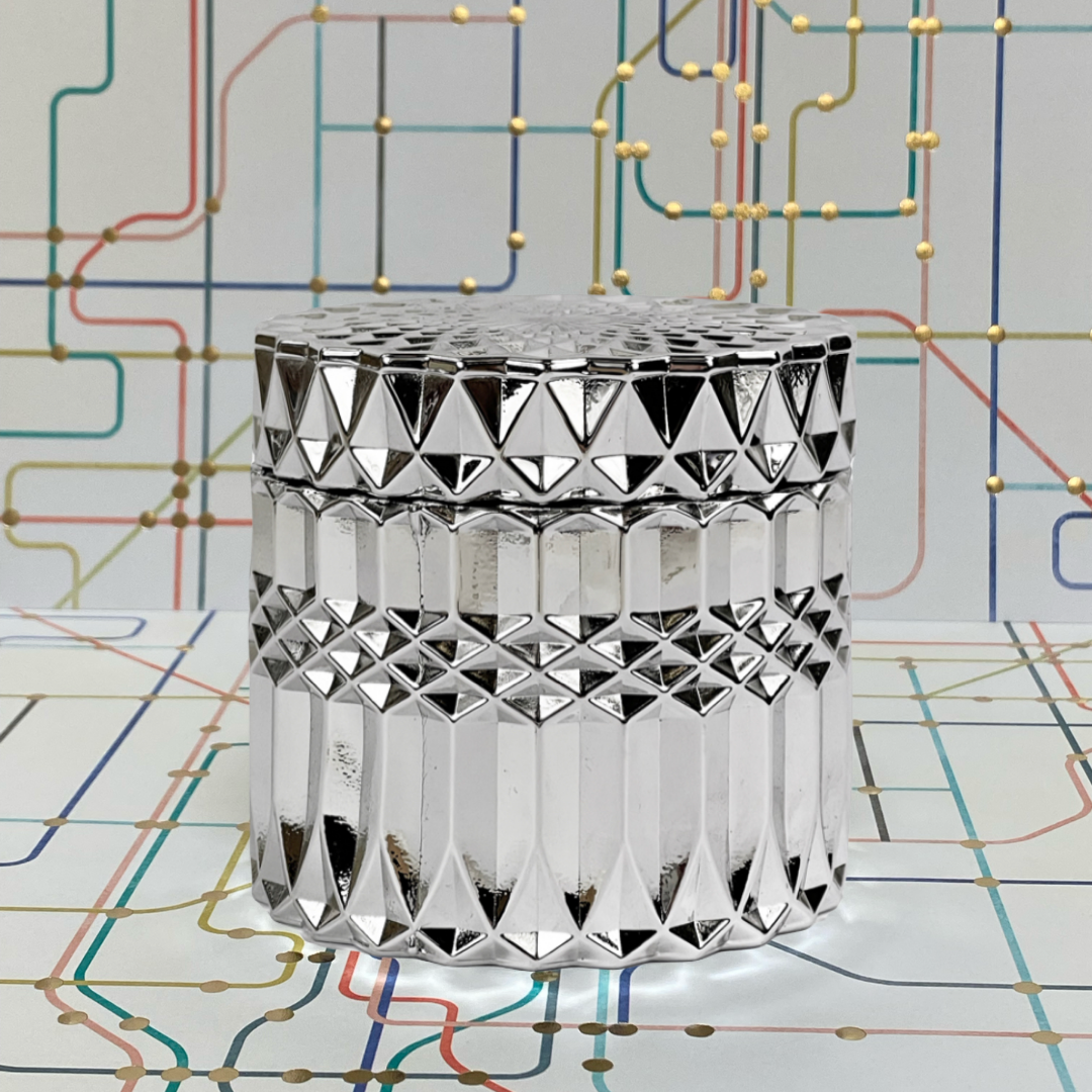 Geometric silver jar with intricate design on colorful abstract background, ideal for home decor or gift.