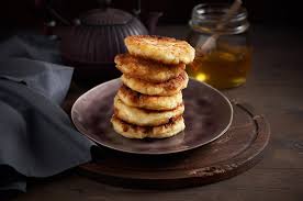 Stack of homemade Ukrainian syrnyky cheese pancakes on a plate, served with honey, showcasing traditional breakfast or dessert option.