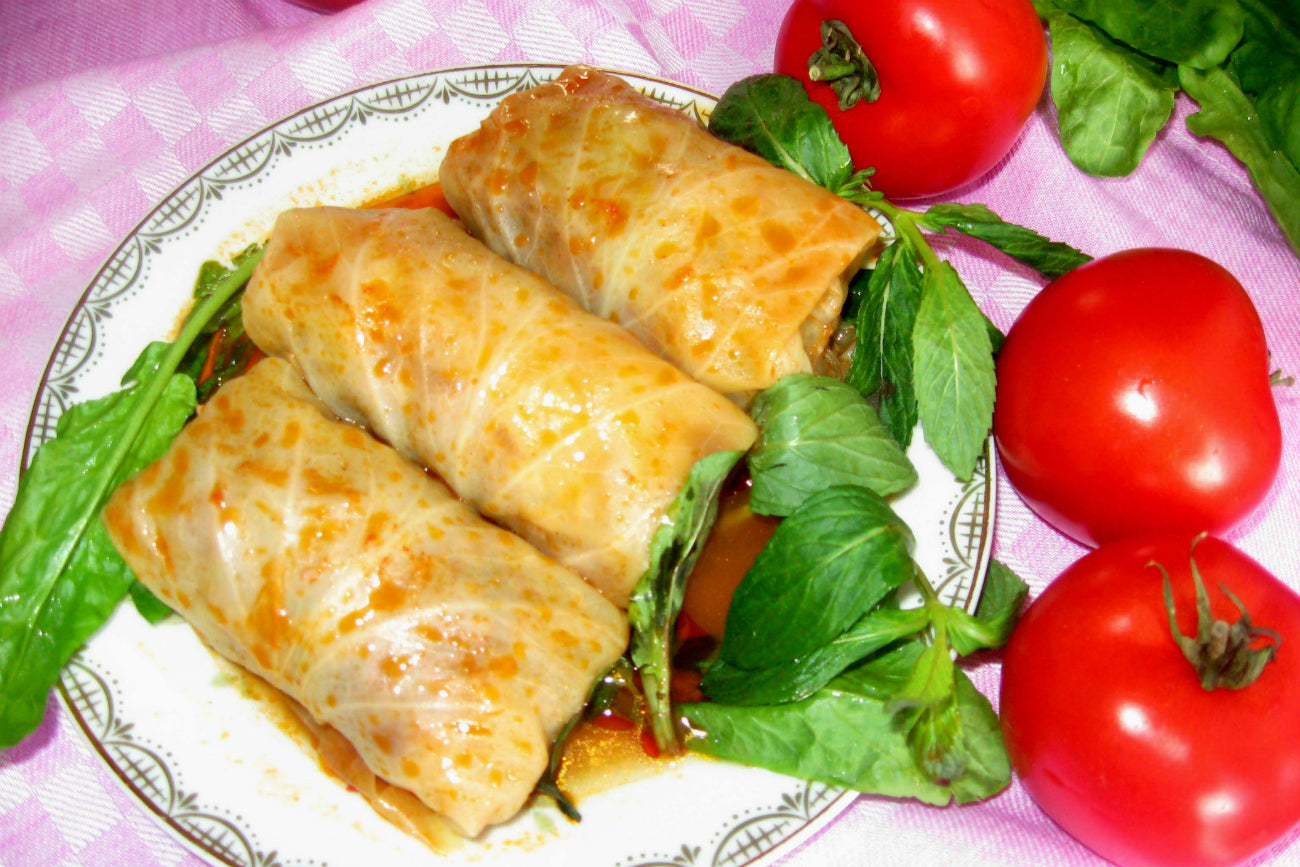 Plate of homemade Ukrainian holubtsi stuffed cabbage rolls with fresh tomatoes on a pink checkered cloth.