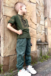 Boy wearing a khaki Ukrainian embroidered Vyshyvanka shirt with geometric patterns, short sleeves, and stand-up collar.