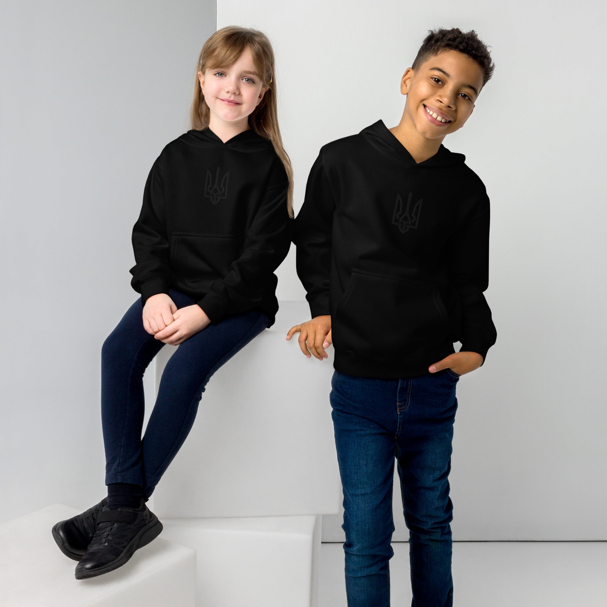 Kids wearing black fleece hoodies with Ukrainian Tryzub design, showcasing soft cotton-poly blend for warmth and comfort.