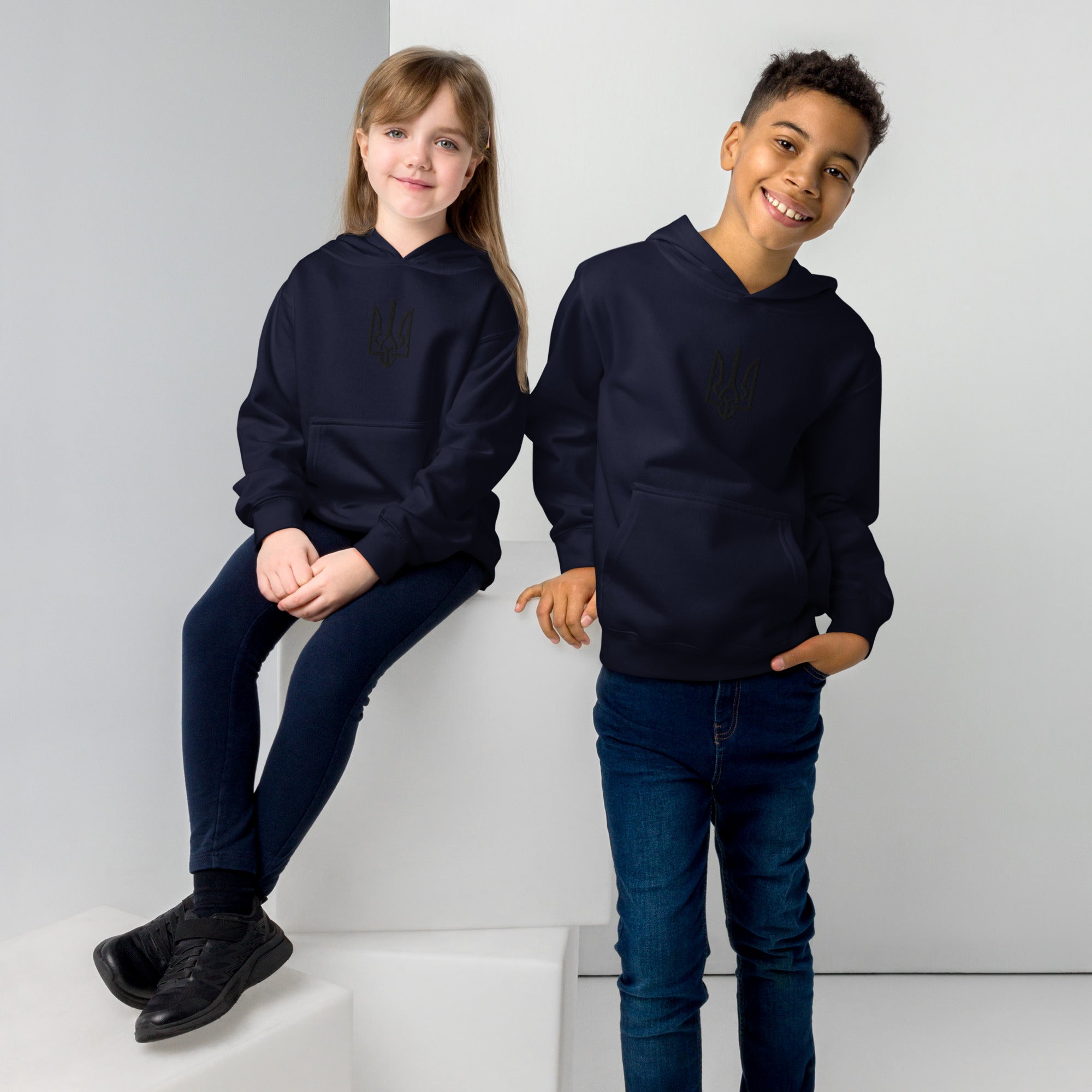 Kids wearing fleece hoodies with Ukrainian Tryzub, smiling and posing, showcasing warmth and style in cotton-poly blend fabric.