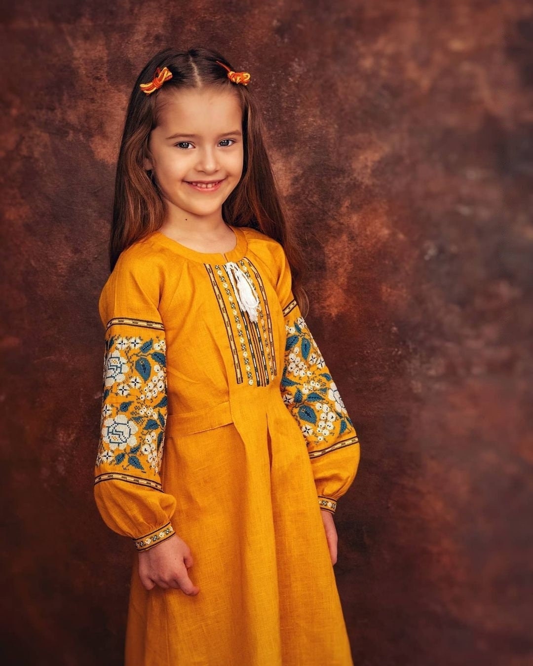 Girl wearing mustard linen Ukrainian embroidered Vyshyvanka dress with floral patterns and long sleeves, cultural and elegant.