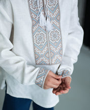 Boy wearing a white vyshyvanka shirt with brown and blue geometric embroidery, featuring traditional Ukrainian cross-stitch patterns.