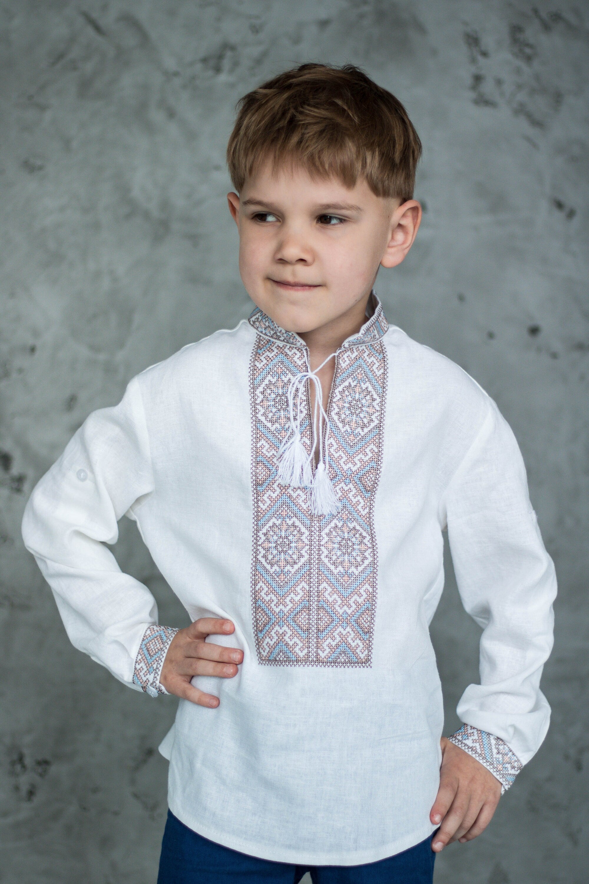 Boy wearing a Ukrainian Vyshyvanka shirt with traditional cross-stitch embroidery in brown and blue on white fabric.