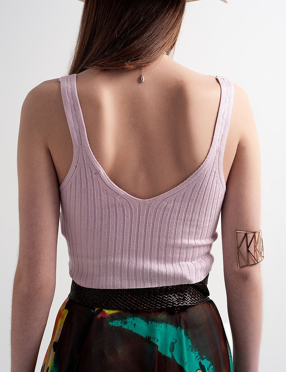 Back view of a woman wearing a soft pink knitted crop top from Evarie, featuring a V-neck and ribbed texture, styled with a colorful skirt.
